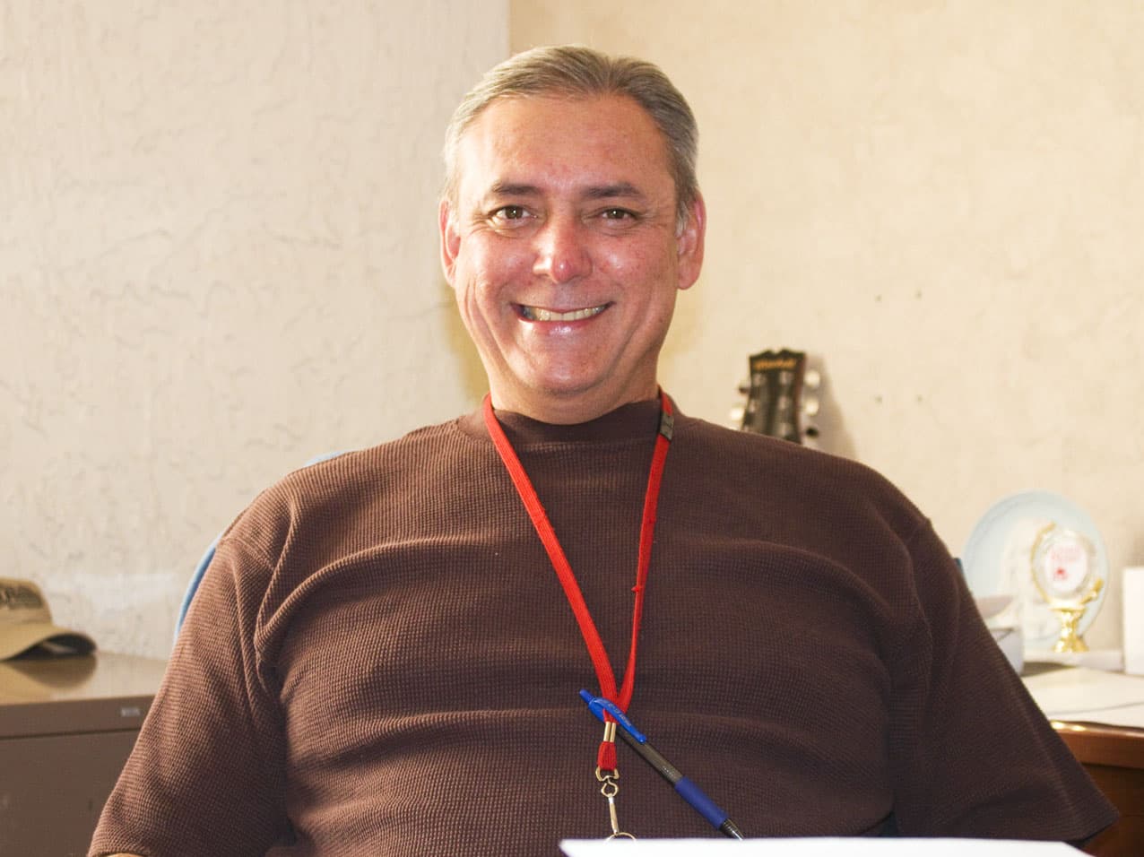 Smiling man with graying hair wearing a brown textured shirt and a red lanyard.